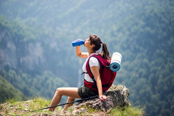 A woman drinking water while resting at the peak of a mountain after a hike